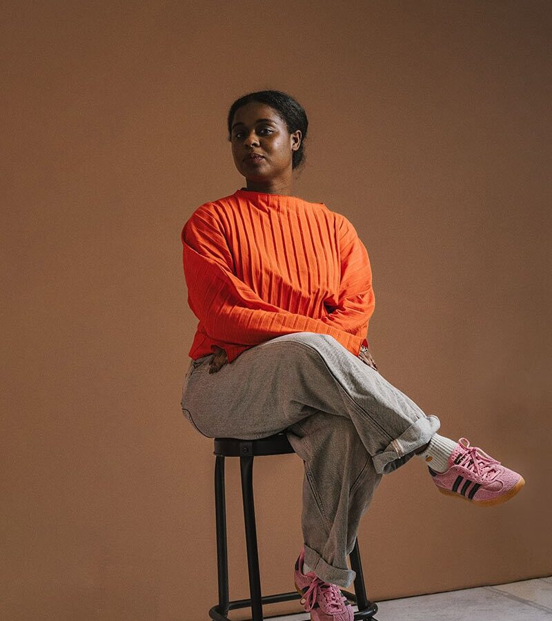 Studio portrait of a Black woman in an orange jumper